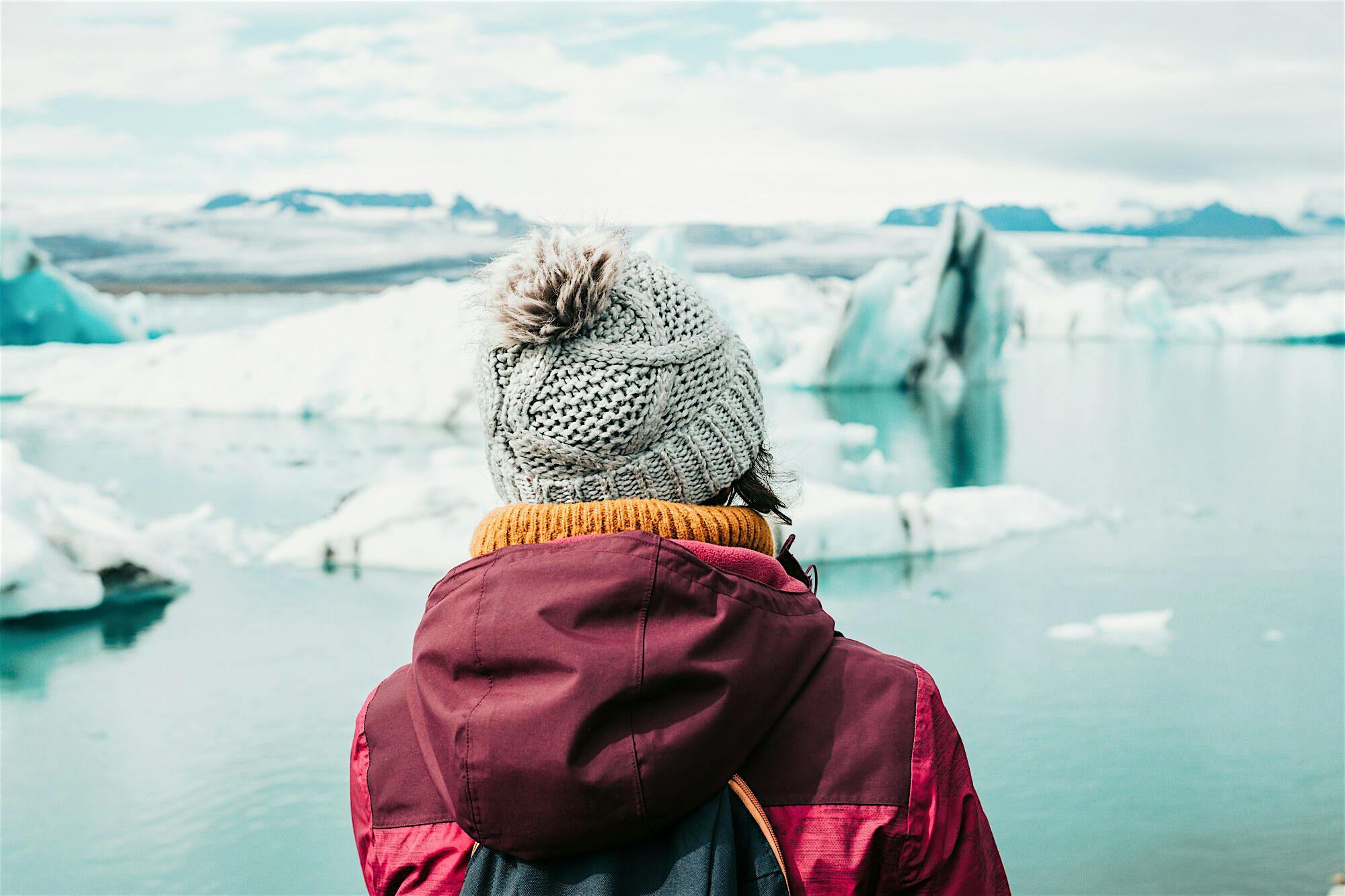 Person in warm clothing looking out at the glacier lagoon with icebergs ahead