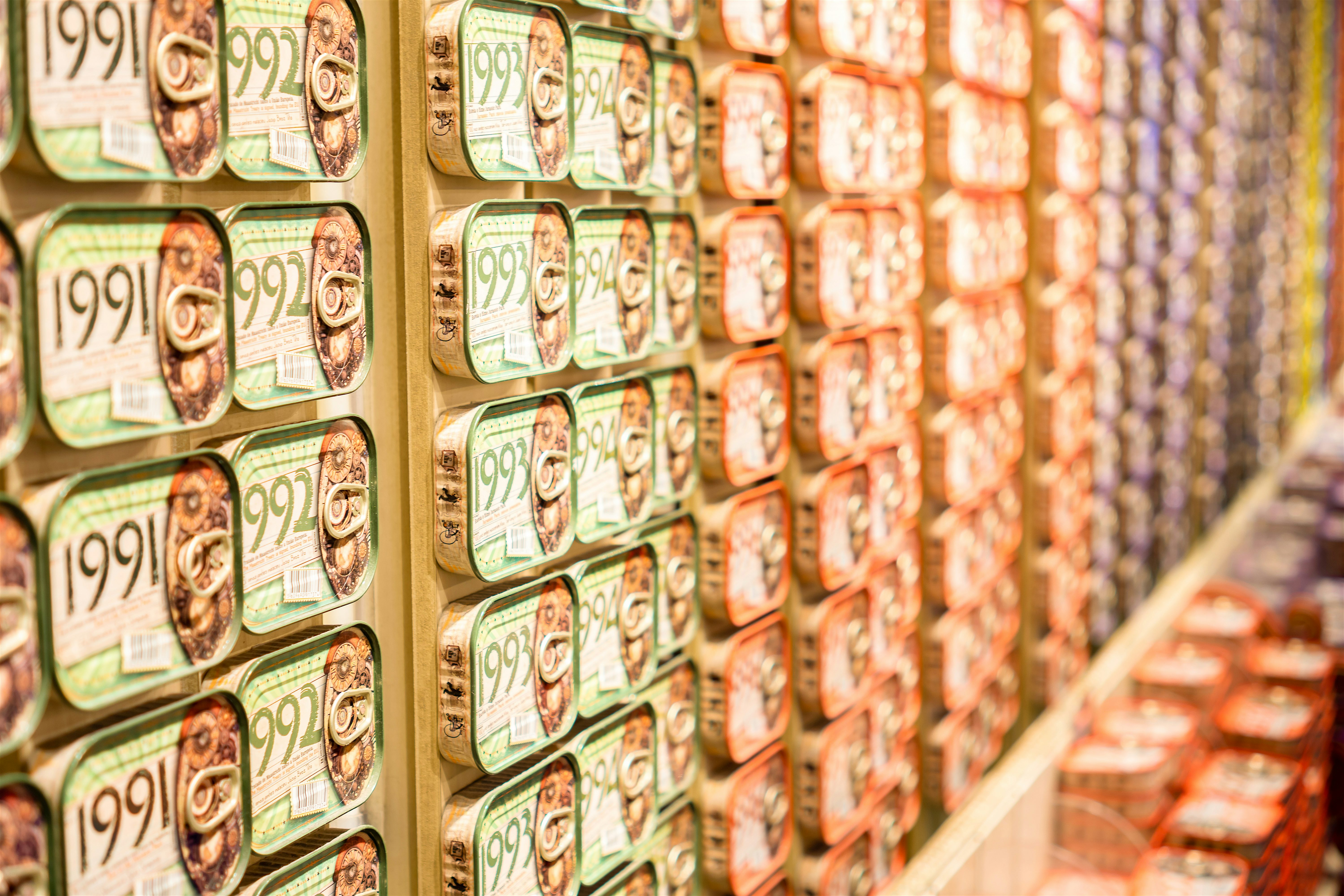 Wall of neatly stacked souvenir tinned fish with illustrated labels, arranged in repeating rows inside a speciality food shop.