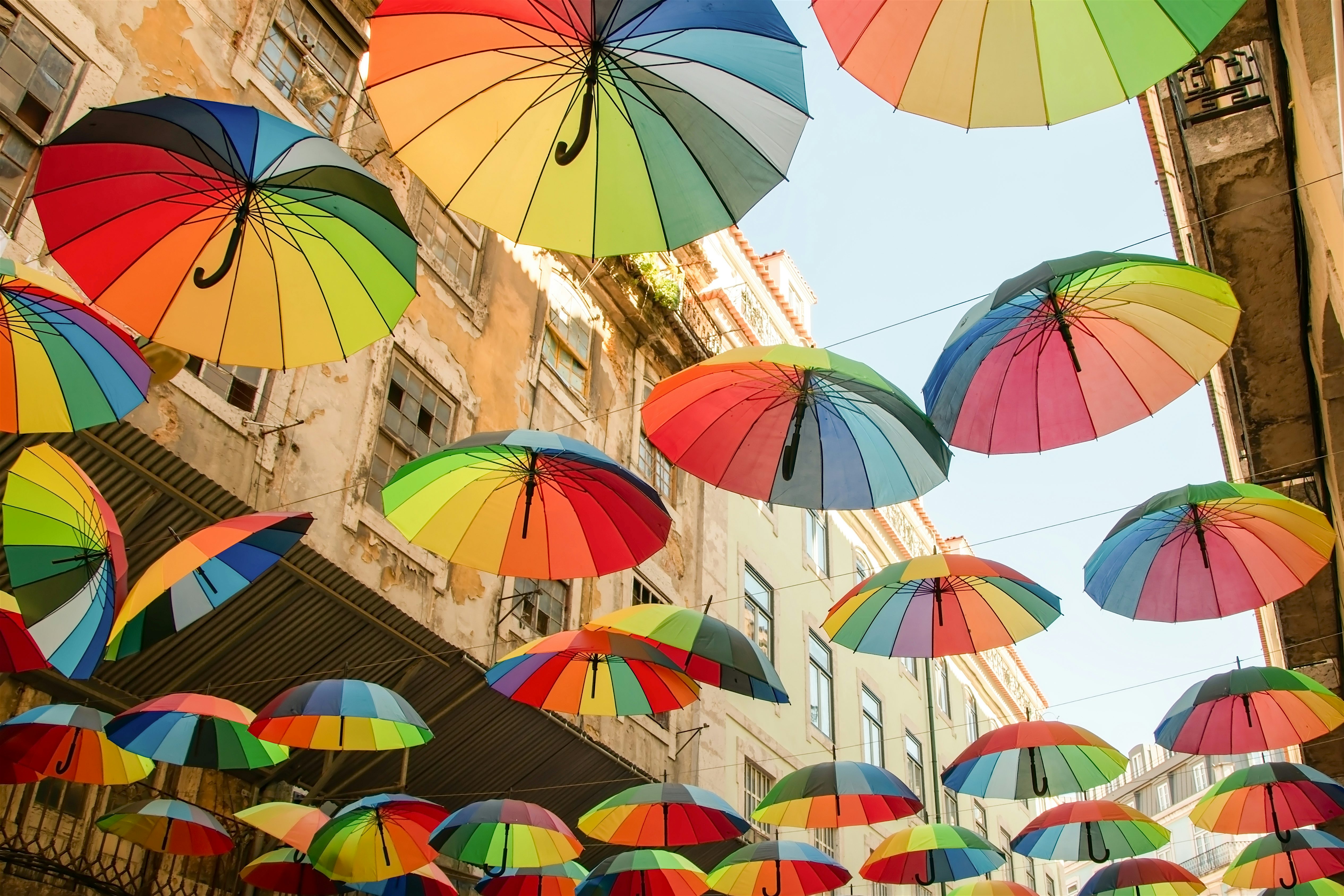 Colourful umbrellas suspended overhead across a narrow street, creating a bright canopy between tall, weathered buildings.