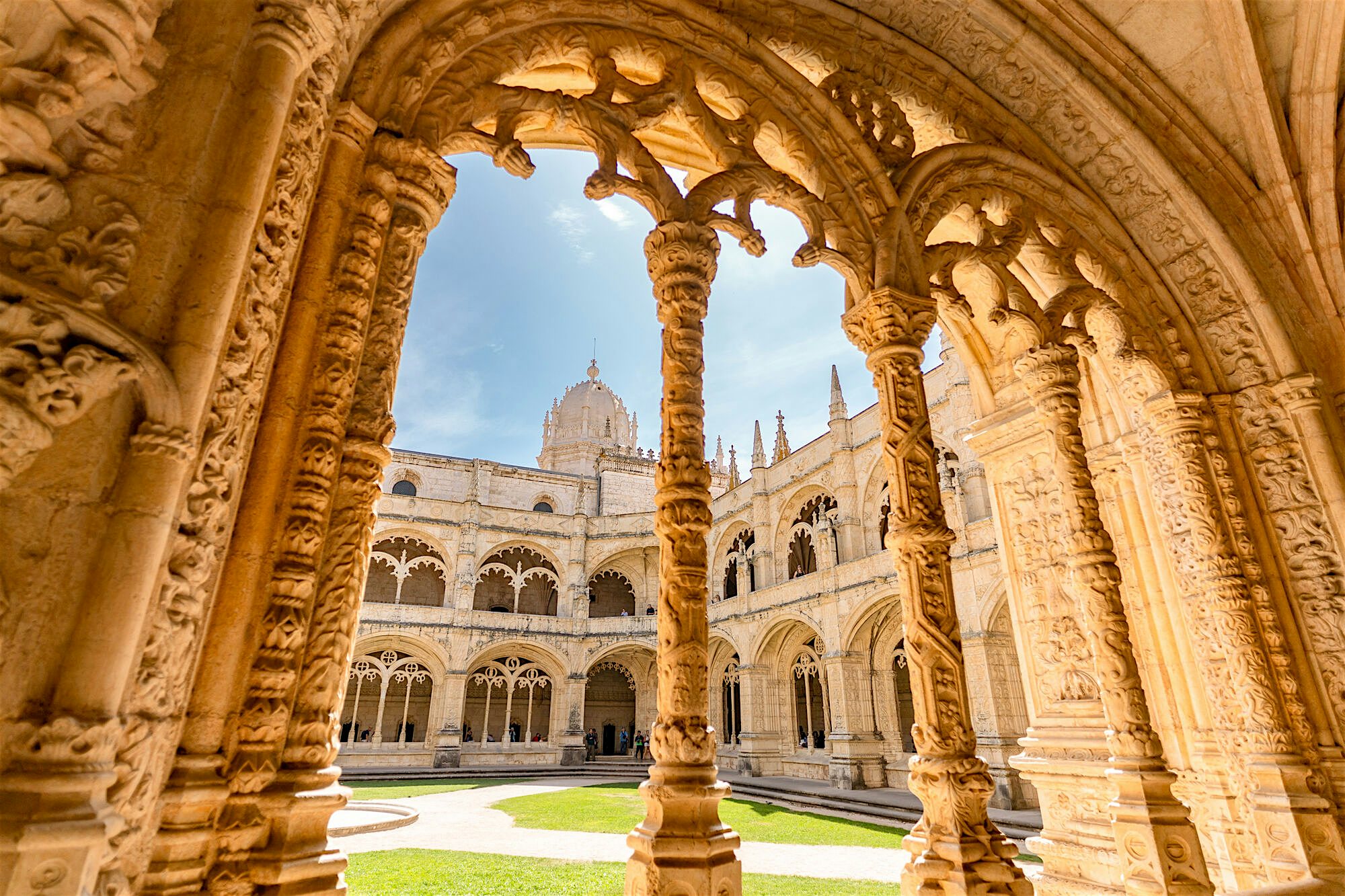Intricately carved stone cloisters framing a peaceful inner courtyard, with arched columns and a domed building visible beyond.