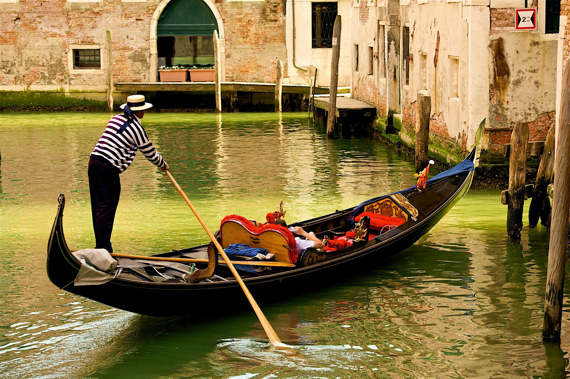 A close up of a traditional gondola ride, one passenger lays in the center of the boat, and the sunligh shines down onto them.