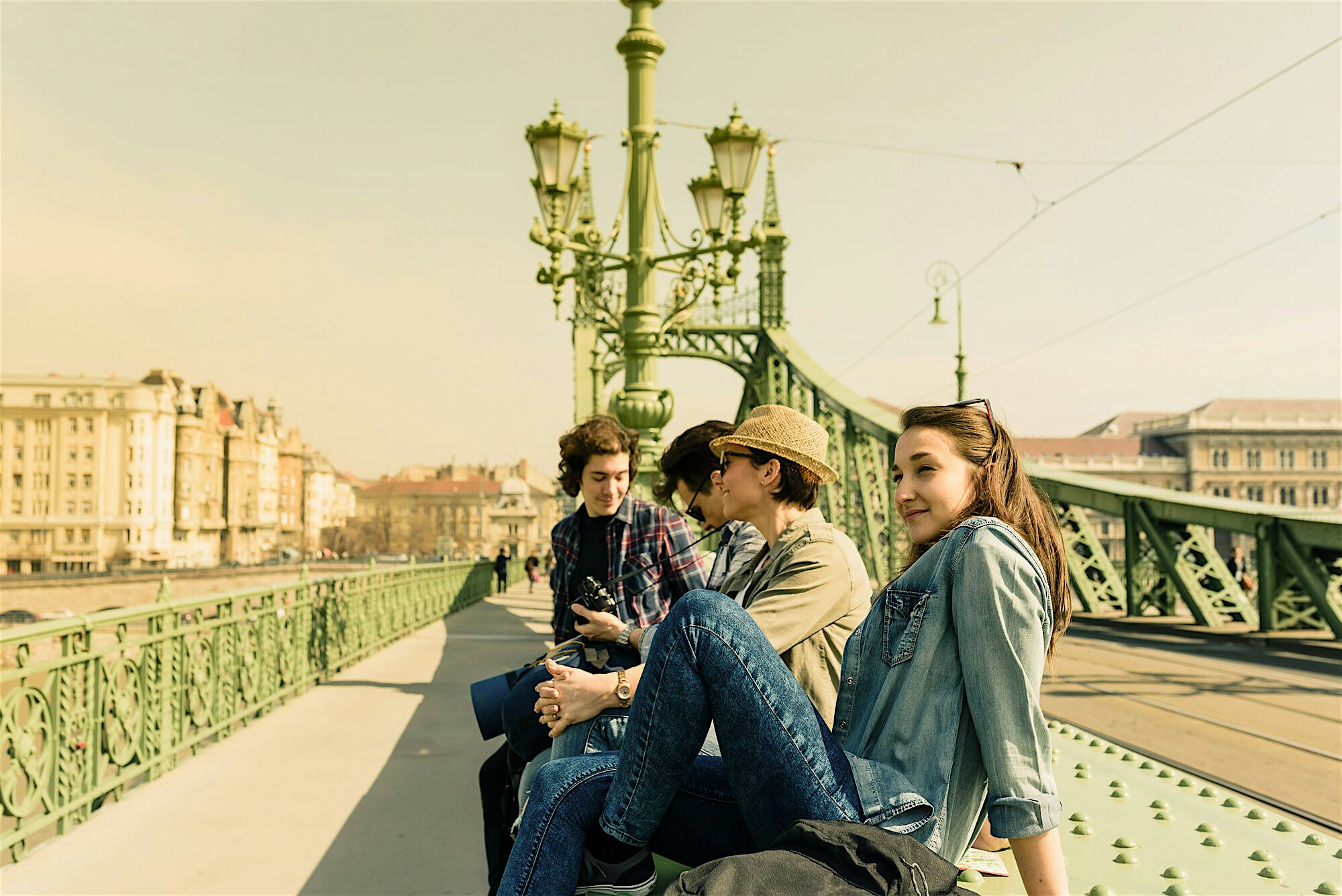 Group of people sat on a bench looking over a bridge.