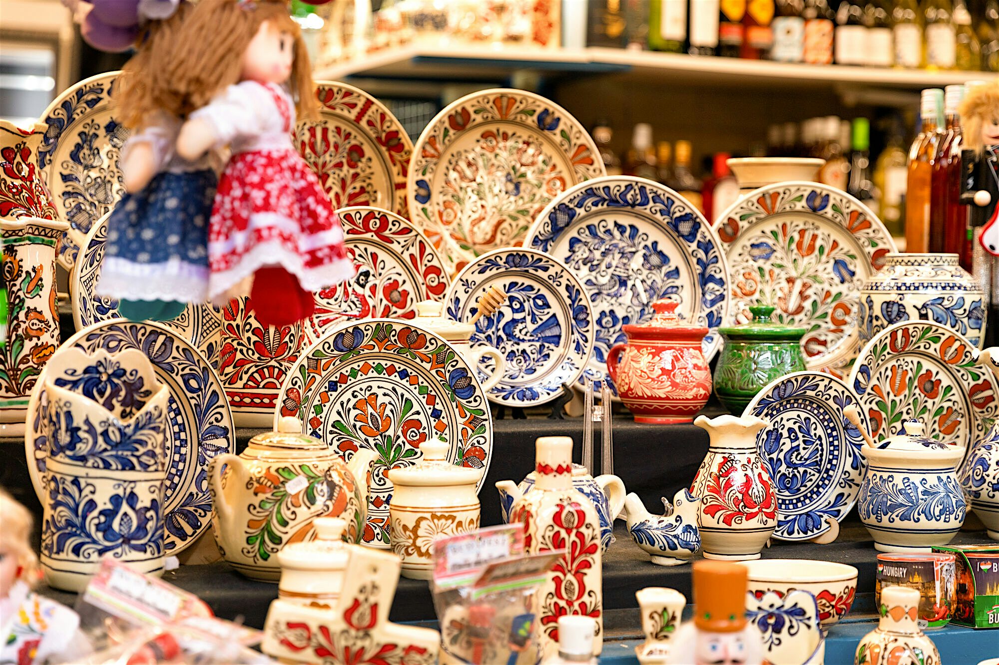 Market display of hand‑painted ceramic plates, jugs, and bowls with intricate red, blue, and green patterns