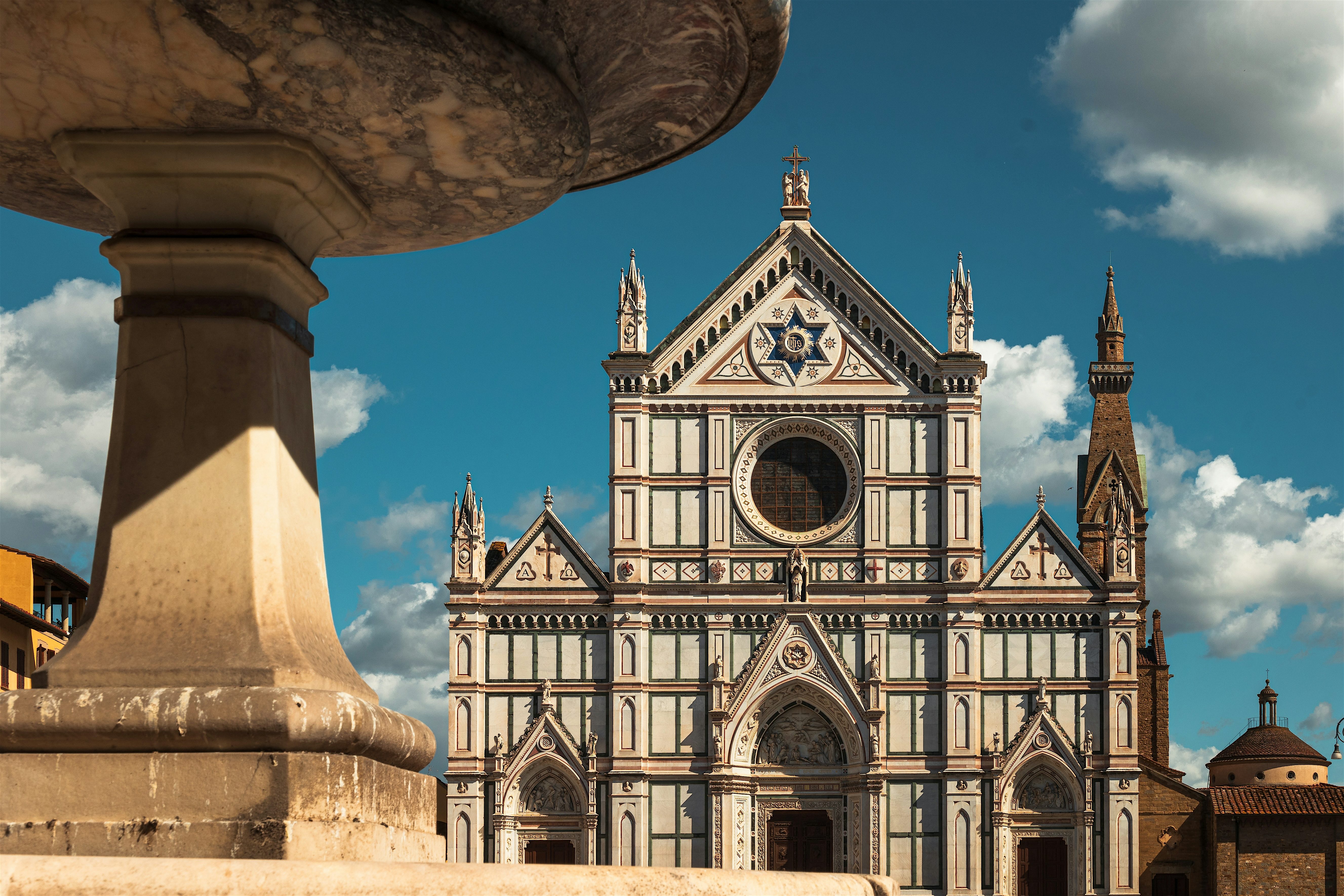 Wide view of Santa Croce in Florence and a stone pillar in forefront with, a blue sky with a few clouds