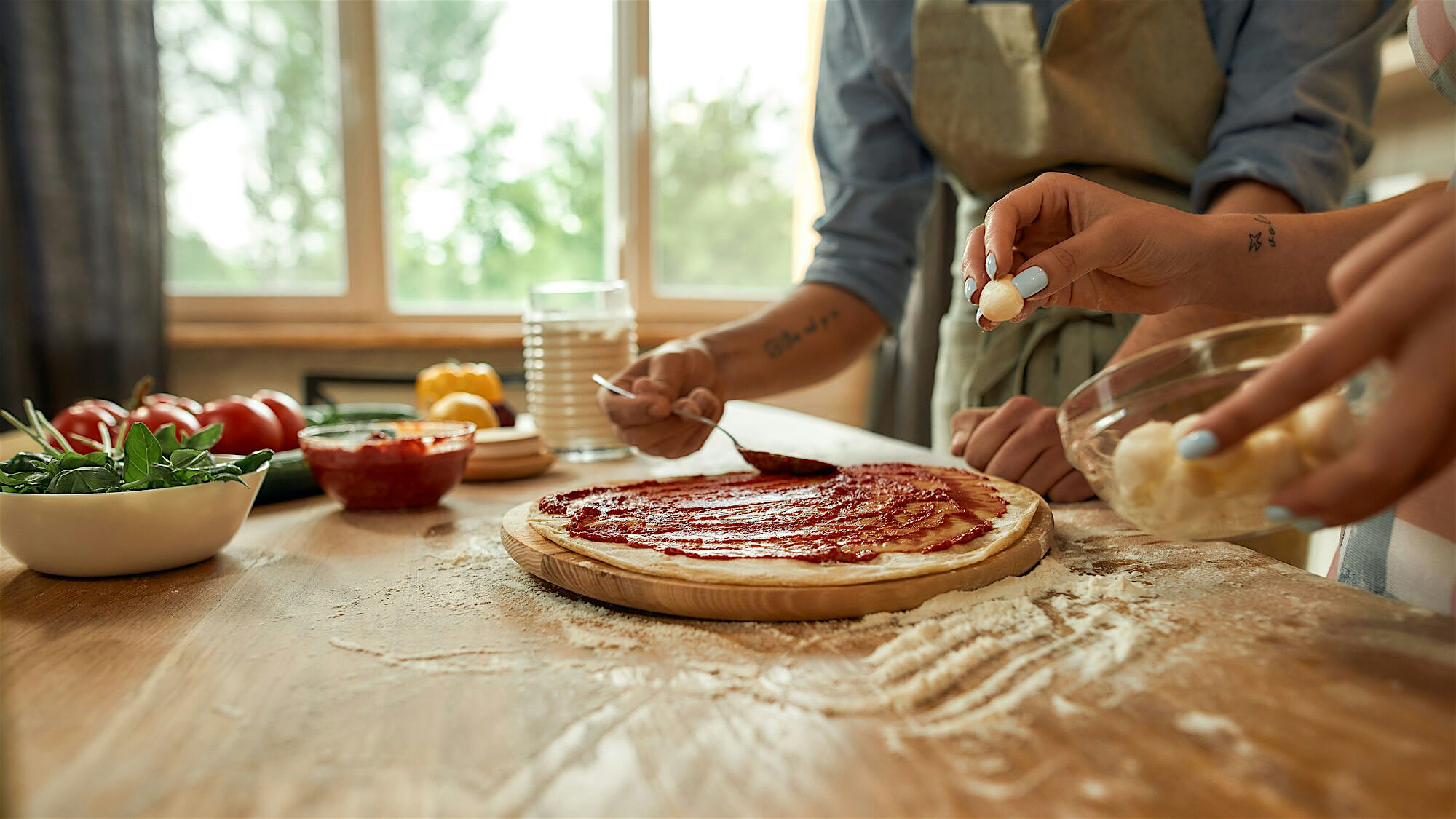 Home made pizza being made, chef spreading tomato sause across a pizza base and topping it with mozerella
