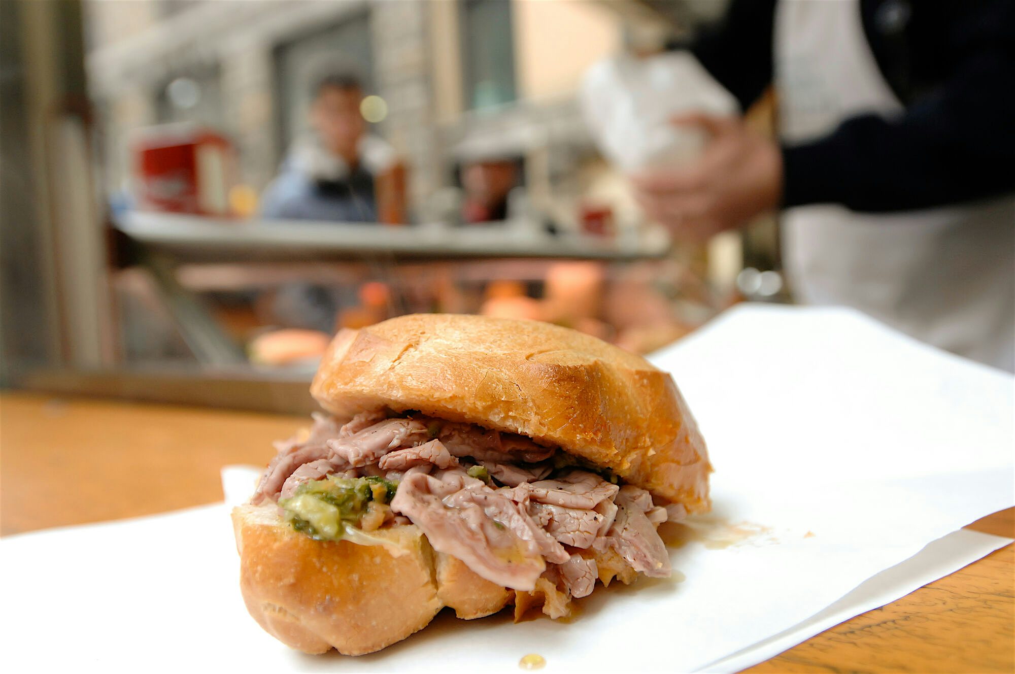 Close up of a beef sandwitch with pickles and meat overflowing inbetween white crusted bread