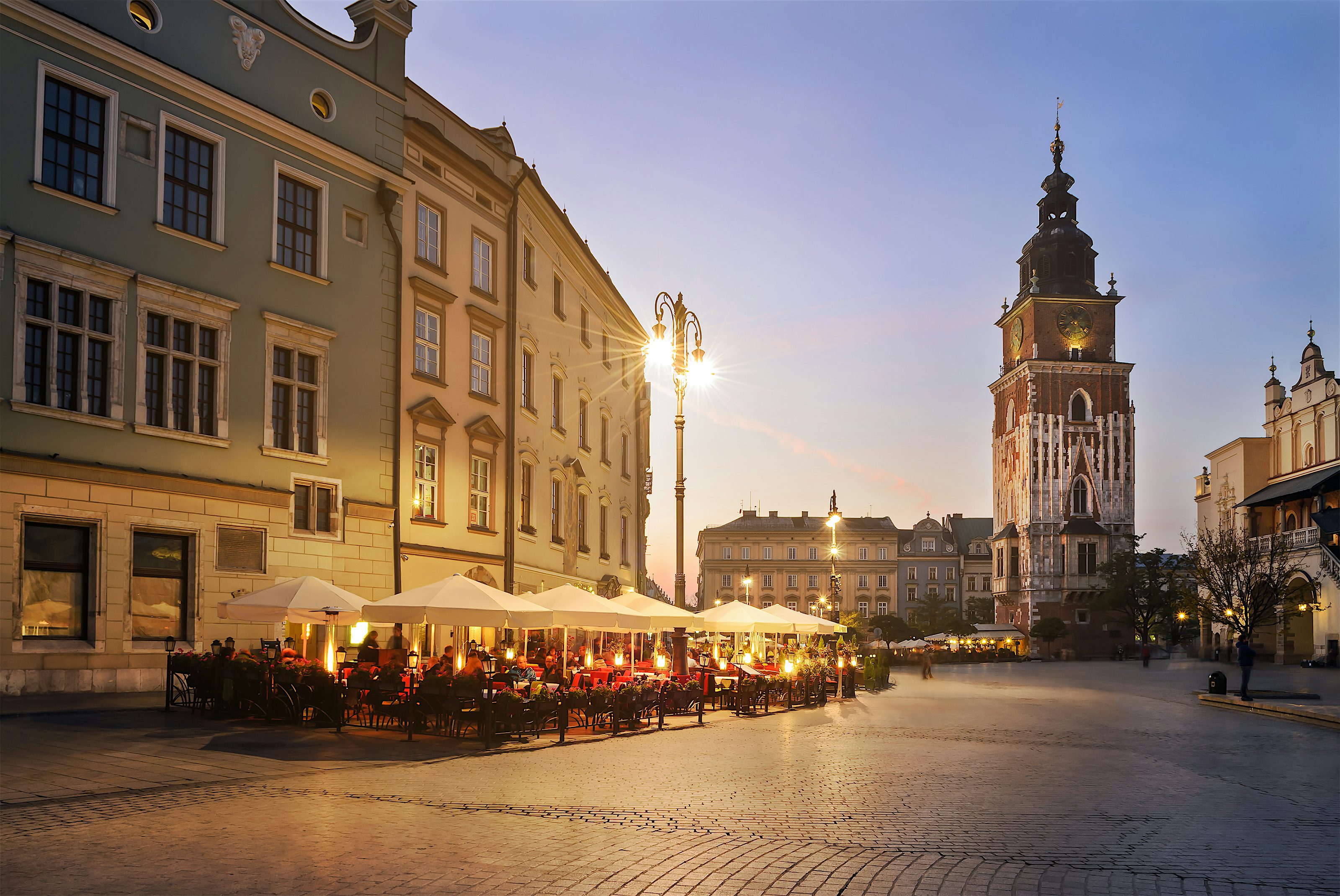 Historic town square at dusk with outdoor café seating under lit umbrellas
