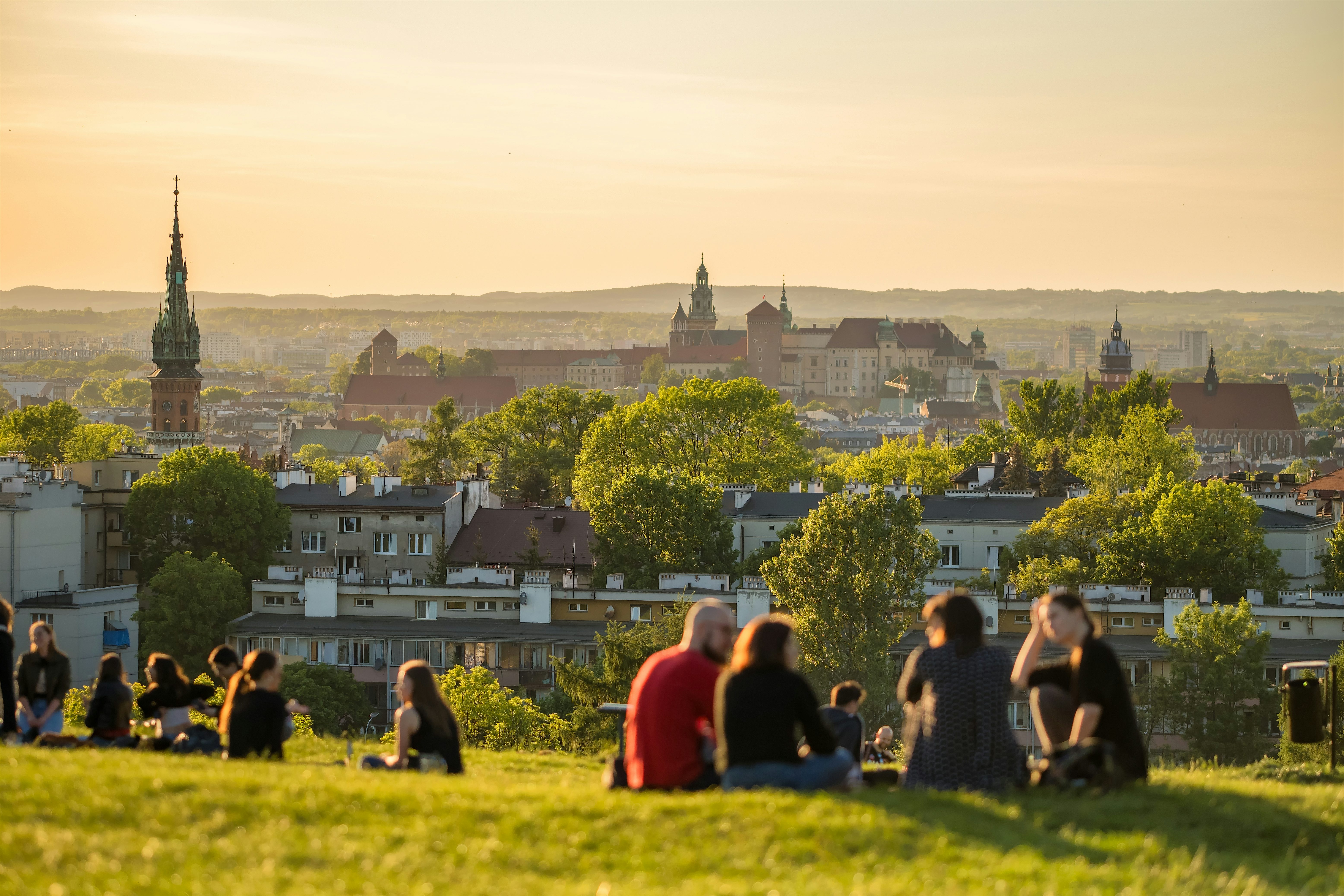People sitting on a grassy hill overlooking a city skyline with church spires and rooftops