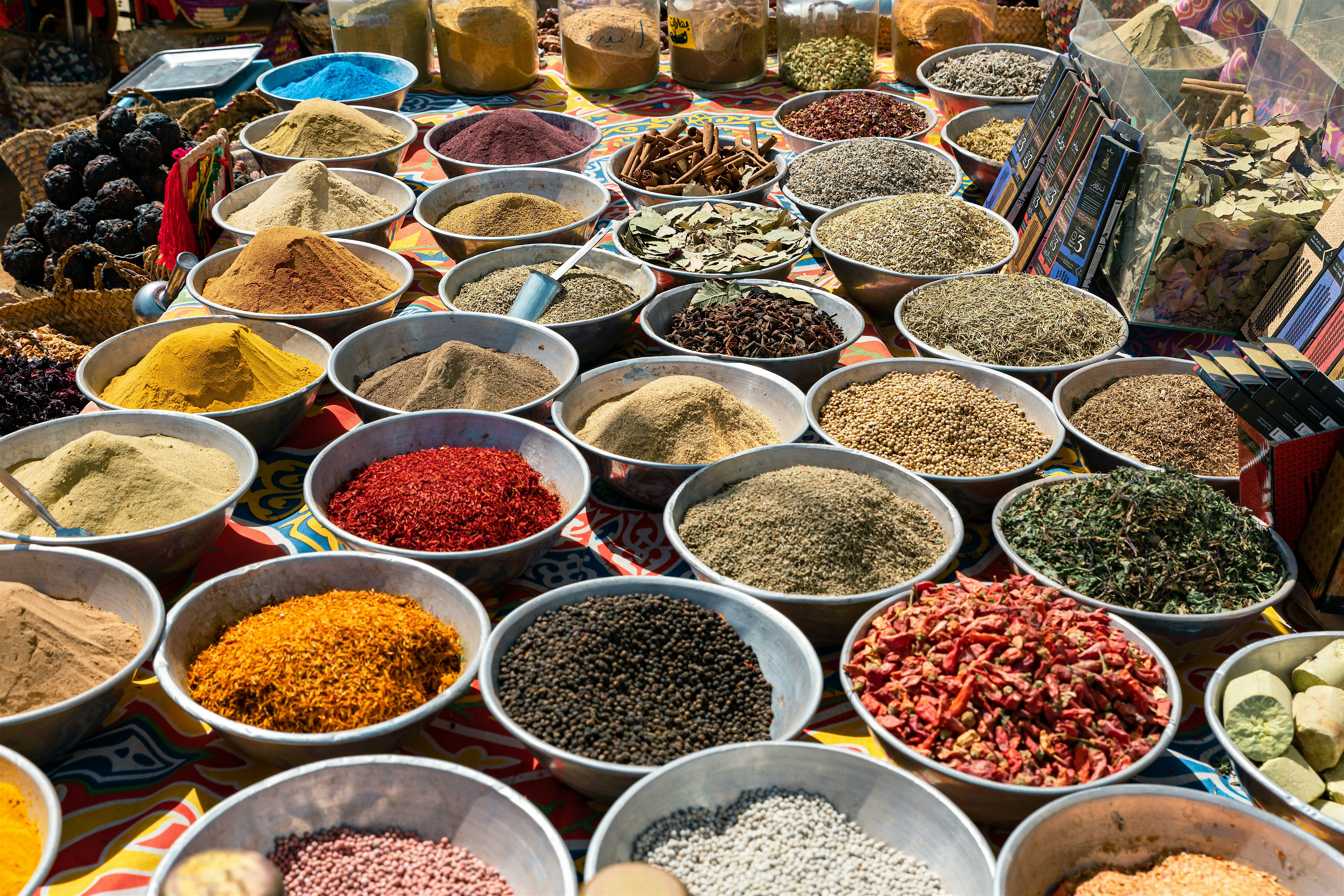 Market display of open bowls filled with colourful spices, herbs, dried flowers, and nuts