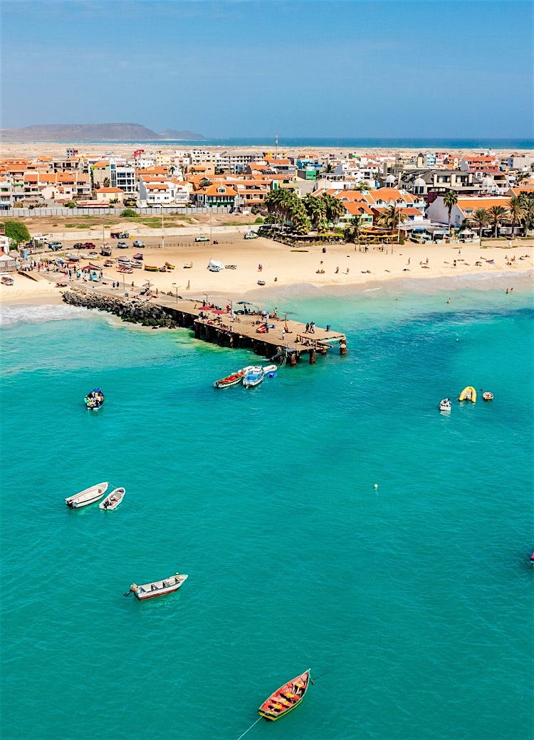 Aerial view of Santa Maria Beach, Sal, Cape Verde, with turquoise ocean, sandy beach, boats, pier, and coastal town.