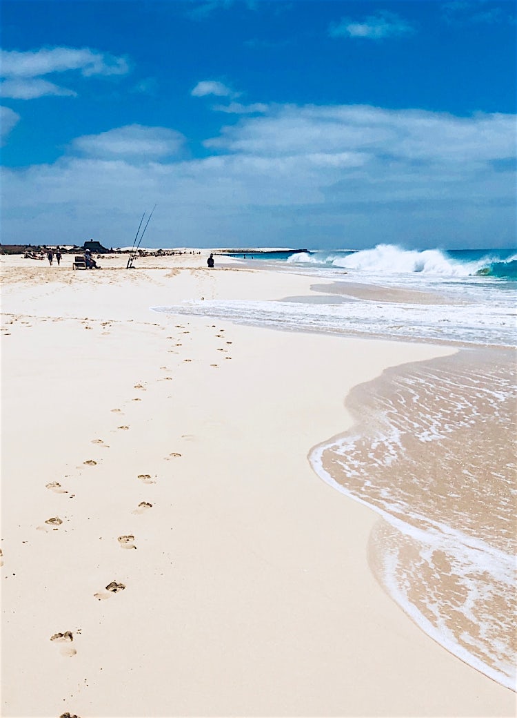 White sand beach in Cape Verde with turquoise Atlantic waves, coastal shoreline, and footprints under a blue sky.