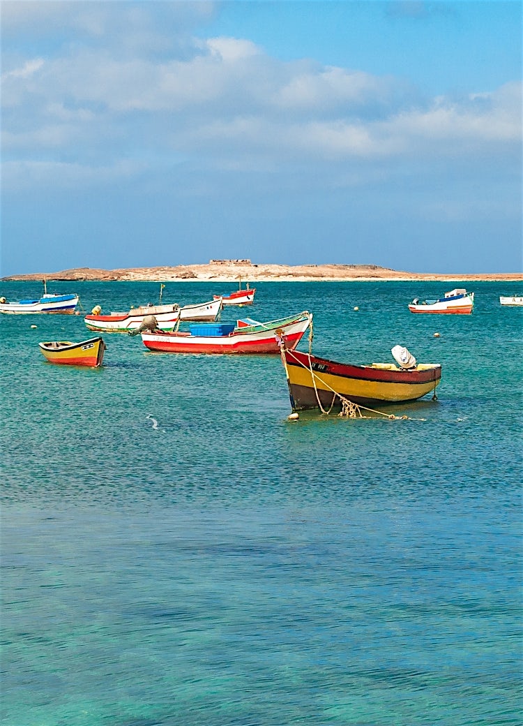 Colorful fishing boats anchored in turquoise waters off Cape Verde with a scenic Atlantic coastline and island backdrop.