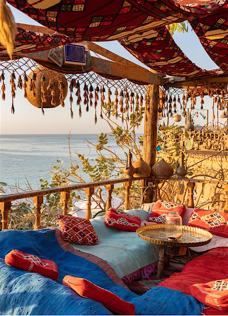 Sandy beach at sunset with straw parasols and sun loungers, framed by yellow flowers.