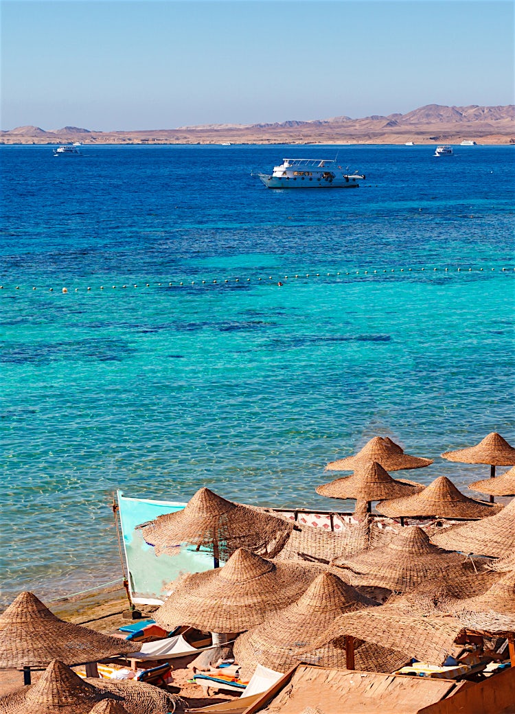 Sharm El Sheikh beach with turquoise Red Sea waters, traditional sun umbrellas and luxury Egyptian seaside resort.