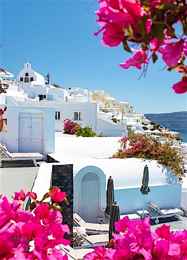 Santorini luxury resort with whitewashed buildings, vibrant bougainvillea flowers and iconic Greek island architecture overlooking the Aegean Sea.