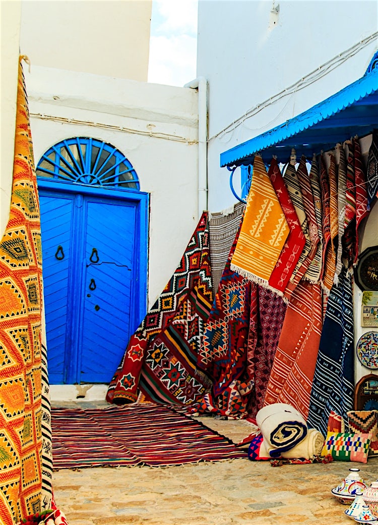 Tunisian market stall with colourful handmade rugs, traditional ceramic plates, vibrant crafts and authentic Medina street scene.