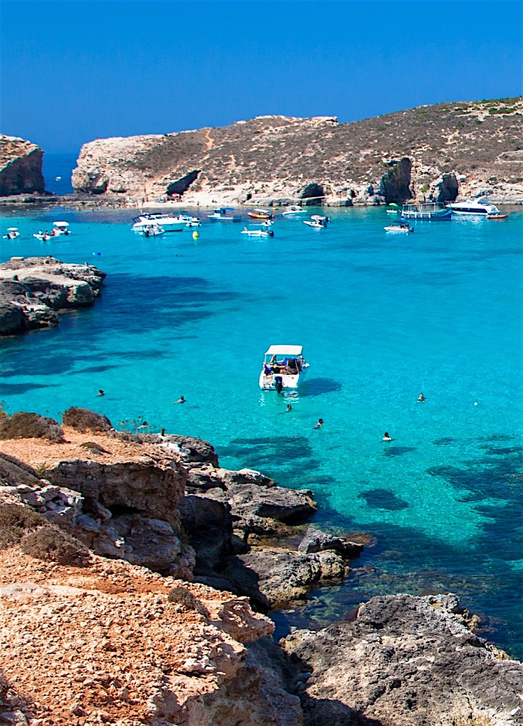 Malta Blue Lagoon with crystal-clear turquoise waters, anchored boats, rocky coastline and Mediterranean island scenery.