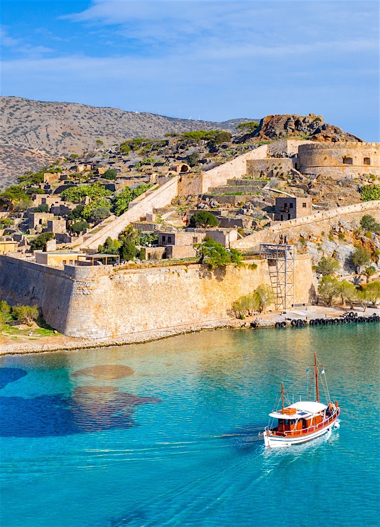 Spinalonga Island fortress in Crete, Greece, with Venetian walls, turquoise sea, coastal mountains and traditional sailing boat.