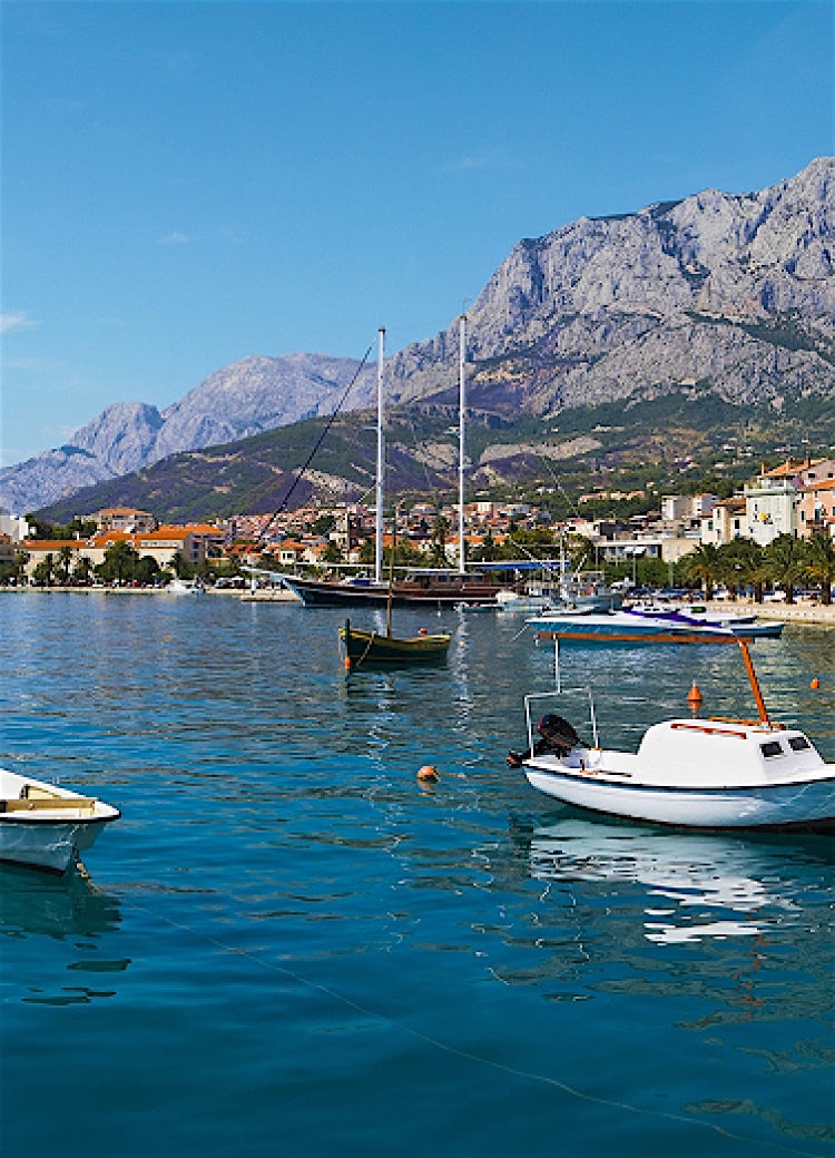 Makarska Riviera, Croatia, with boats on the Adriatic Sea, waterfront promenade, and the Biokovo Mountains rising above the coastal town.