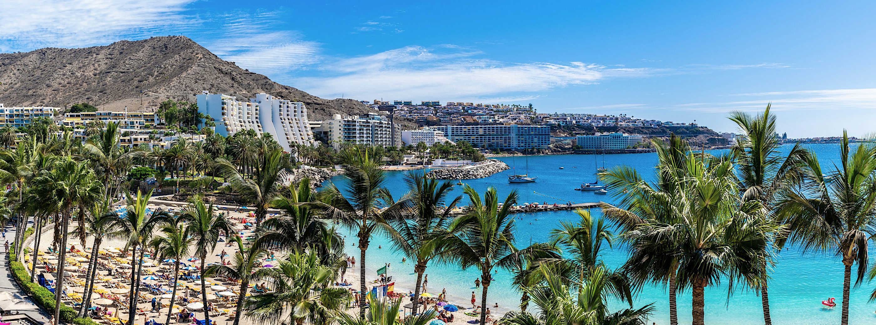 Gran Canaria beachfront resort with palm trees, golden sands, turquoise Atlantic waters, luxury hotels, and a scenic coastal bay.
