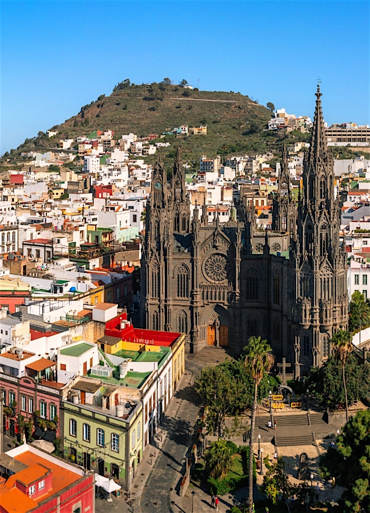 Panoramic view of Las Palmas de Gran Canaria featuring Santa Ana Cathedral, colourful historic buildings and coastal hillside scenery.