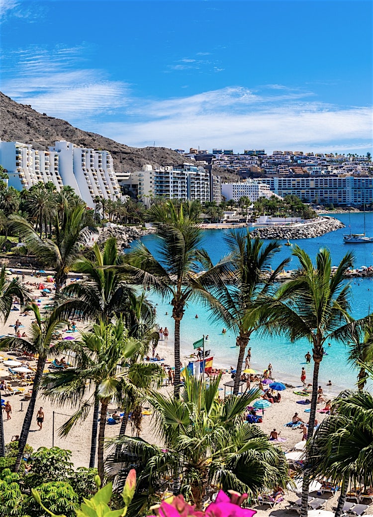 Gran Canaria beachfront resort with palm trees, golden sands, turquoise Atlantic waters, luxury hotels, and a scenic coastal bay.
