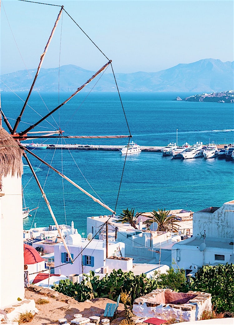 Mykonos windmill overlooking a marina with luxury yachts, whitewashed buildings and panoramic Aegean Sea views.
