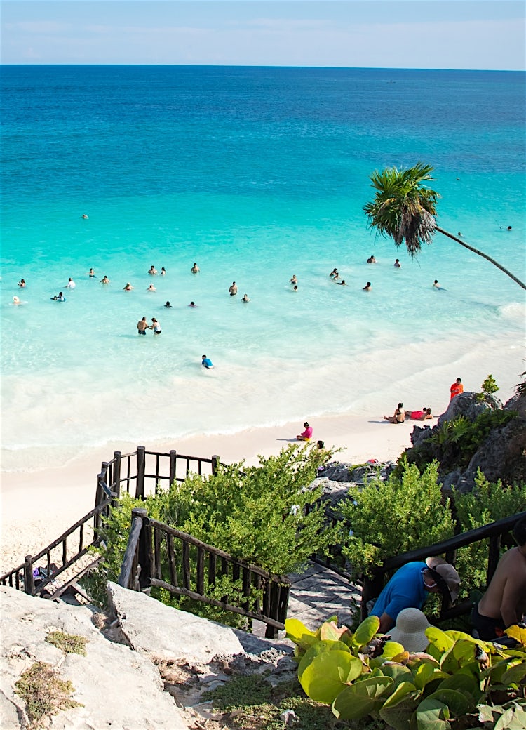 Tropical Caribbean beach with turquoise ocean, white sand shoreline, swimmers in crystal-clear water, and palm trees overlooking a popular coastal destination.