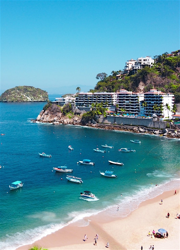 Mexico beach resort with turquoise bay, anchored boats, sandy shoreline, coastal hotels, and scenic Pacific Ocean views.