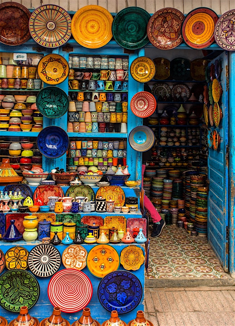Traditional Moroccan pottery shop displaying colourful handmade ceramics, decorative plates, tagines, and artisanal crafts in a vibrant market setting.