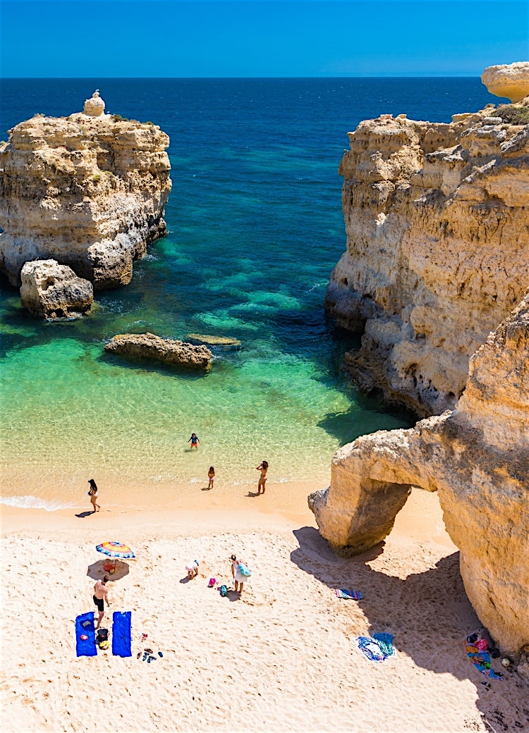 Algarve beach in Portugal with golden limestone cliffs, turquoise Atlantic waters, secluded sandy cove, and dramatic coastal rock formations.