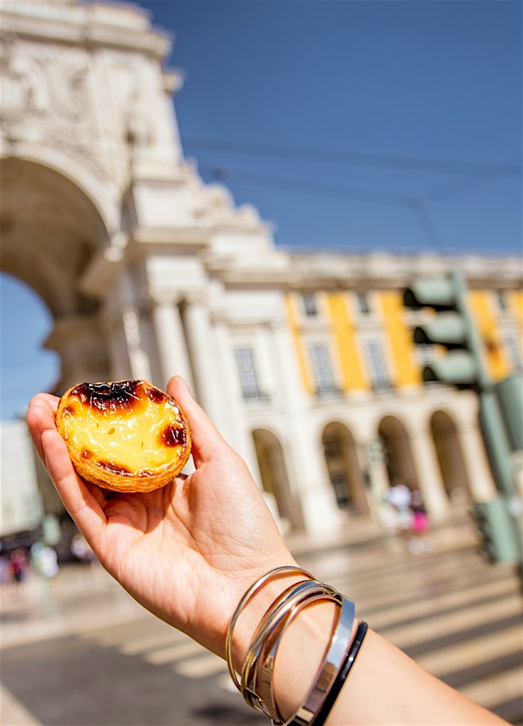 Traditional Portuguese pastel de nata held in Lisbon’s Praça do Comércio, with historic architecture and city landmarks in the background.