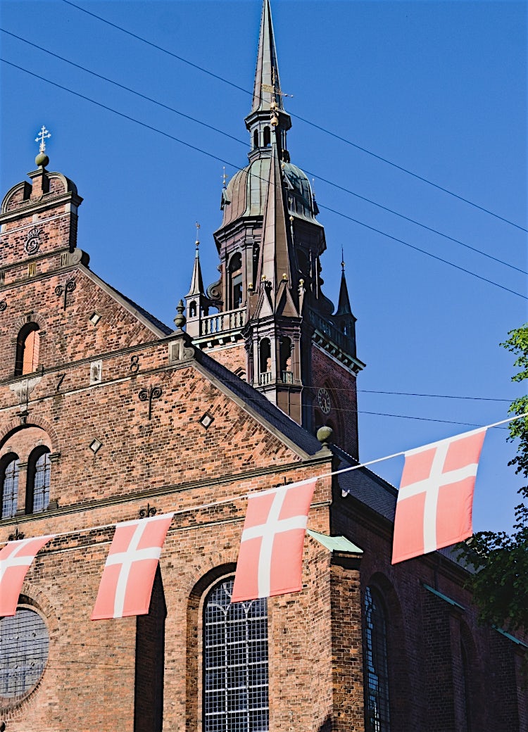 Copenhagen historic church in Denmark with red-brick architecture, Danish flags, and traditional cityscape under a clear blue sky.