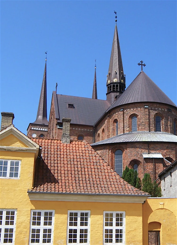 Roskilde Cathedral in Denmark, featuring historic Gothic brick architecture, soaring spires, and colourful traditional Danish buildings.