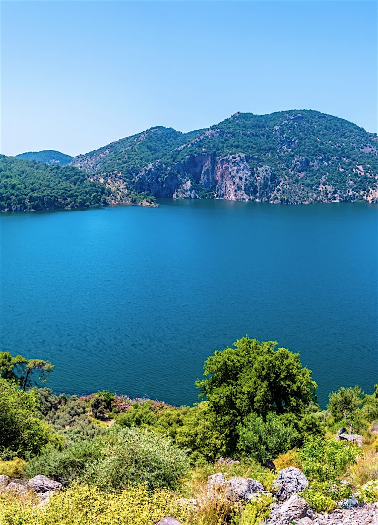 Dalaman lake and mountain landscape in Turkey, featuring crystal-clear blue waters, forested hills, and scenic natural countryside views.Boat anchored in a small bay