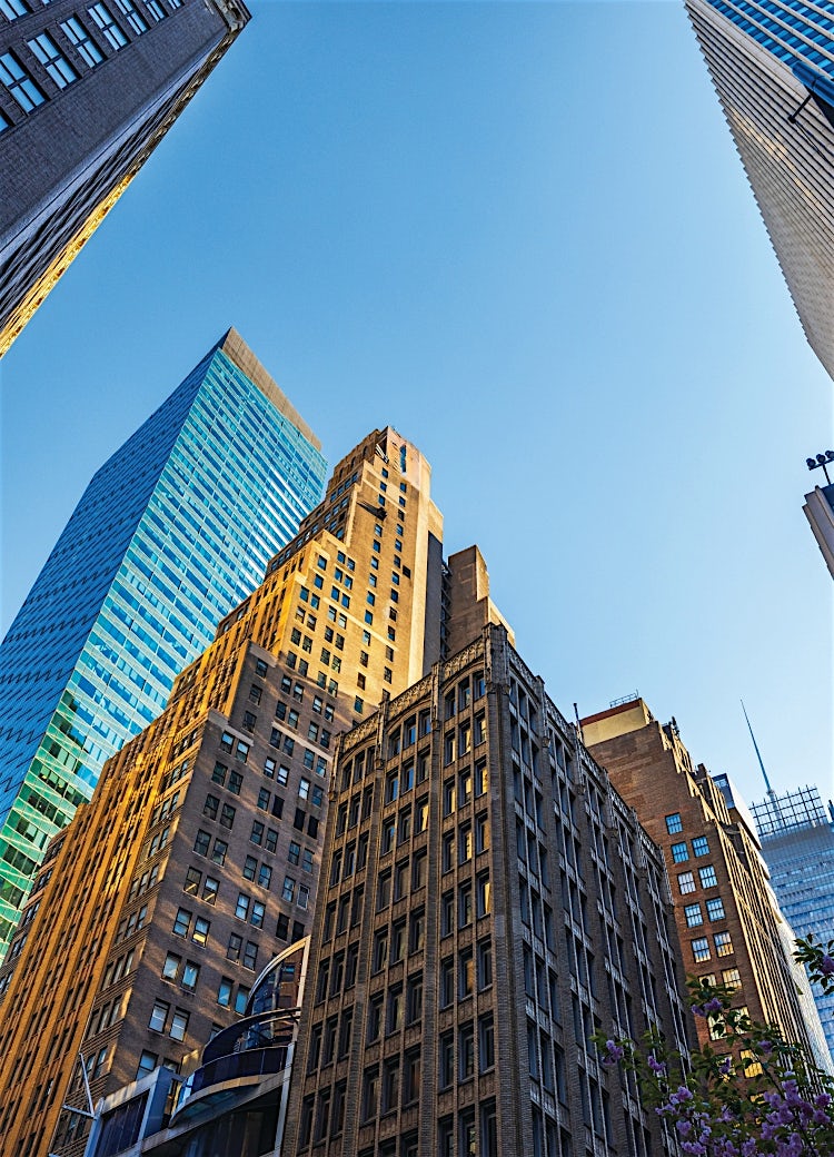 New York City skyline with modern skyscrapers, glass office towers, and iconic Manhattan architecture viewed from street level.