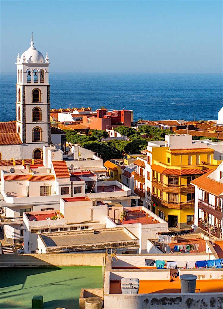 Canary Islands coastal town with historic church tower, colourful buildings, Atlantic Ocean views, and volcanic island scenery.