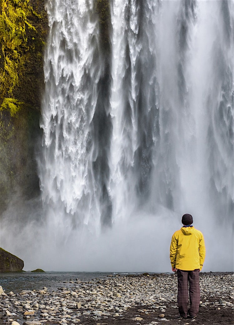 Skógafoss waterfall in Iceland, featuring cascading water, dramatic cliffs, misty spray, and a visitor admiring the natural landscape.