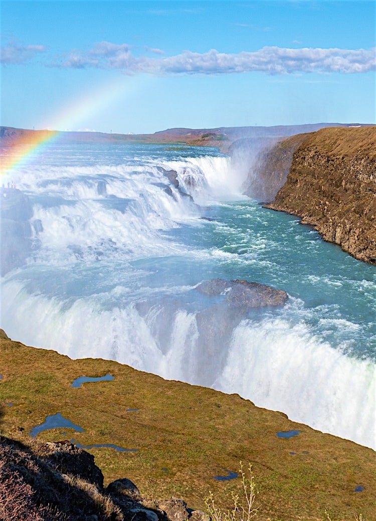 Gullfoss waterfall in Iceland with cascading glacial waters, dramatic canyon scenery, and vibrant rainbow over the falls.