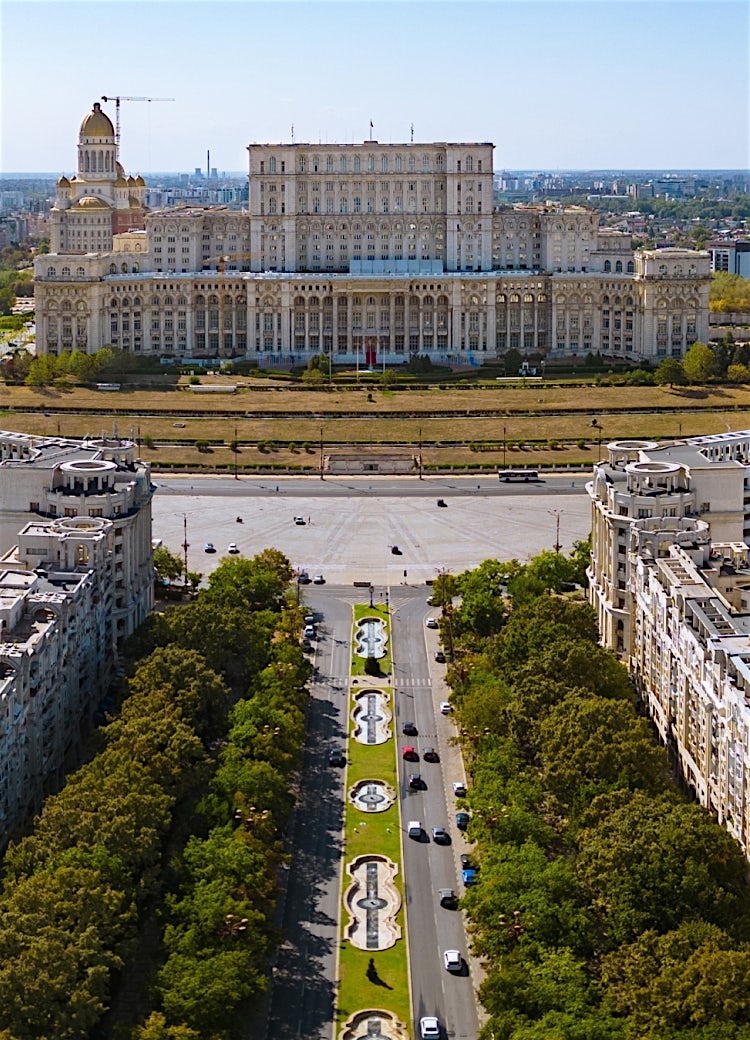 Palace of the Parliament, Bucharest, Romania, viewed from Unirii Boulevard with landscaped fountains and city skyline.