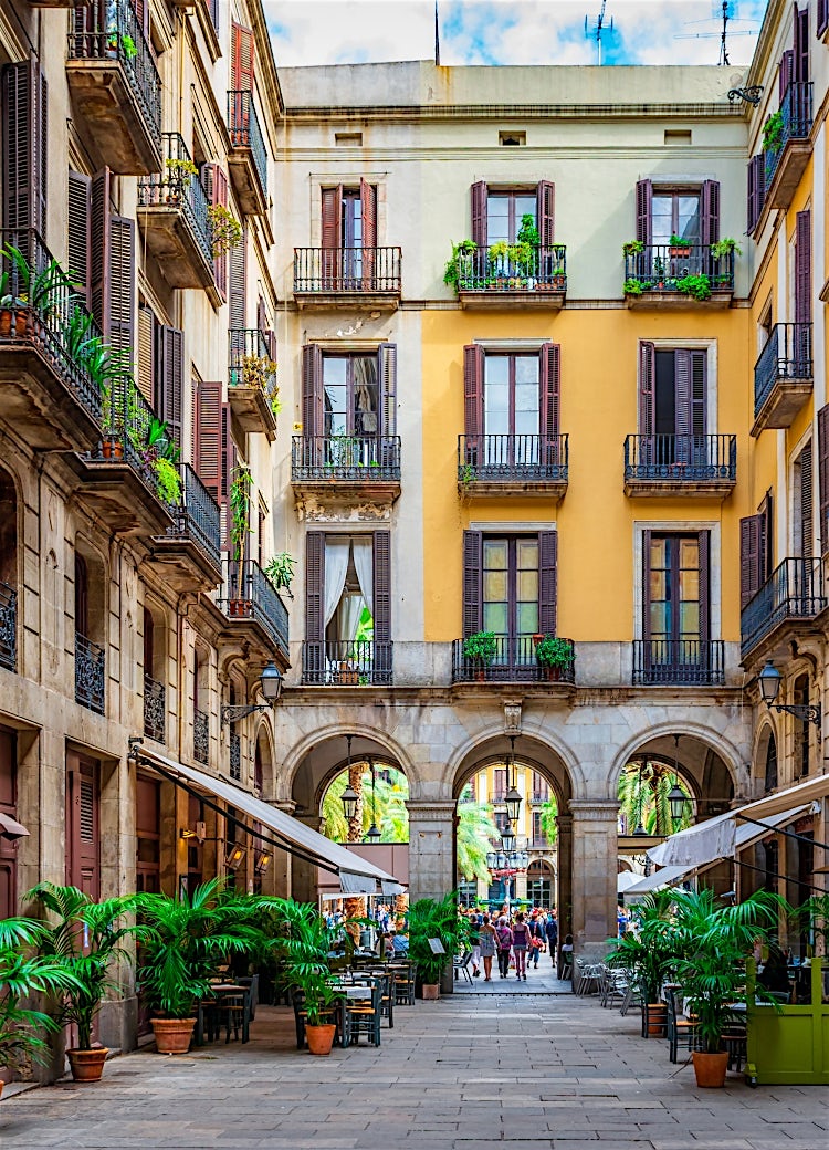 Historic Gothic Quarter courtyard in Barcelona, Spain, featuring colourful residential façades, wrought-iron balconies, stone archways and a charming pedestrian street lined with potted plants.