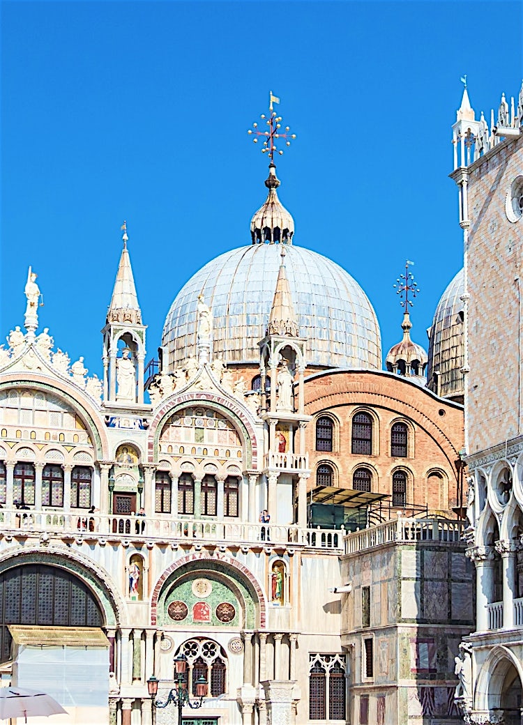 St Mark’s Basilica and Doge’s Palace in Venice, Italy, showcasing ornate Venetian Gothic architecture, domes, arches and historic city landmark facades under a clear blue sky.