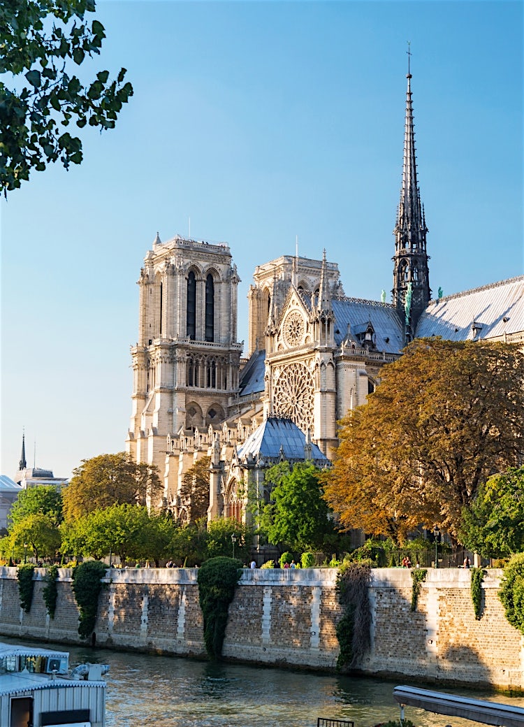 Notre-Dame Cathedral in Paris, France, viewed from the River Seine, showcasing iconic Gothic architecture, historic towers and riverside scenery.
