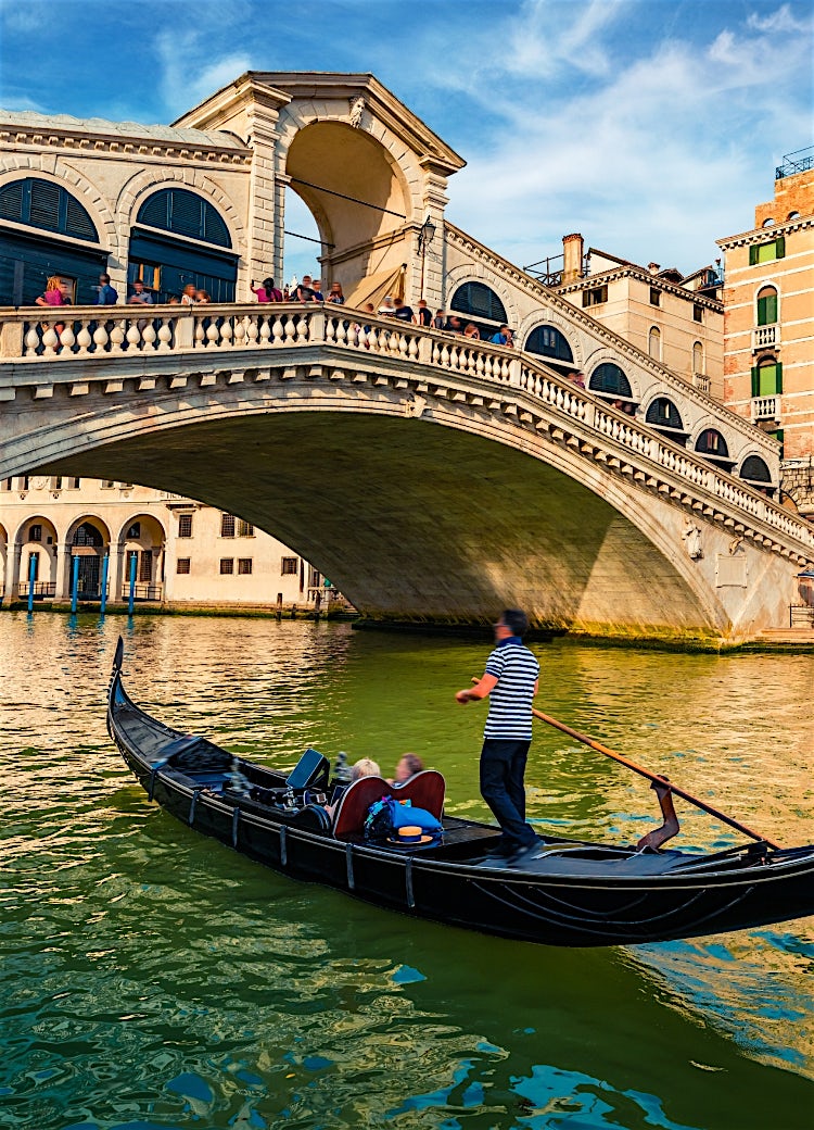 Gondola passing beneath Venice’s historic Rialto Bridge on the Grand Canal, showcasing iconic Venetian architecture and waterfront scenery.