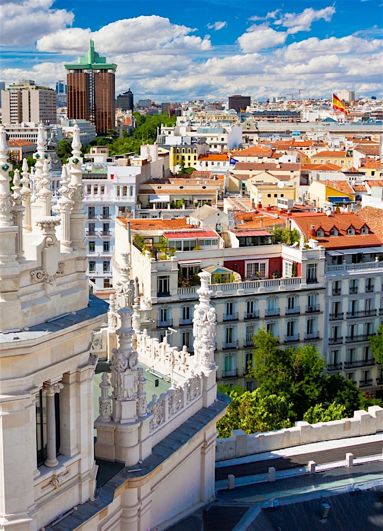 Madrid skyline viewed from Cibeles Palace, featuring ornate white architecture, historic city buildings, tree-lined boulevards and panoramic views across Madrid, Spain.