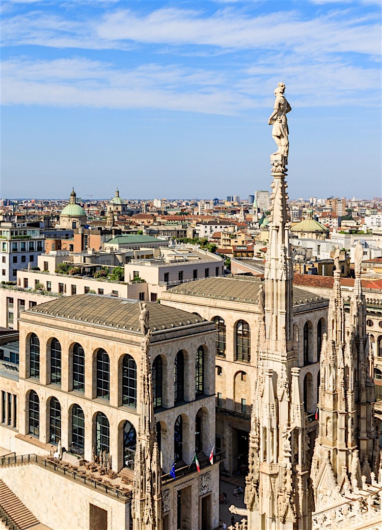 Milan skyline viewed from the rooftop of Duomo di Milano, featuring intricate Gothic spires, historic architecture and panoramic city views across Milan, Italy.