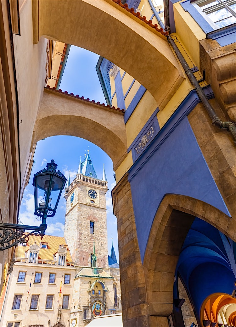 Prague Old Town archway framing the Gothic Old Town Hall Clock Tower, with historic pastel buildings and blue sky in the Czech capital.