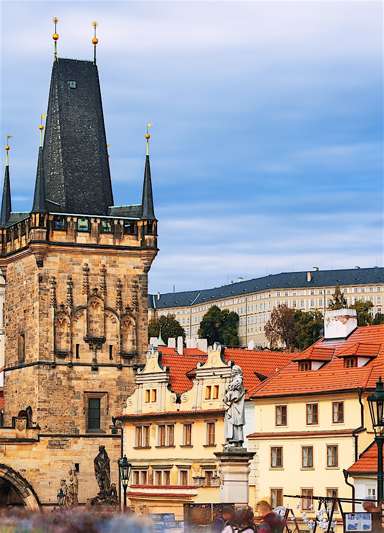 Prague skyline with Charles Bridge towers, red-tiled rooftops, St. Nicholas Church dome, and Prague Castle overlooking the historic Czech capital.