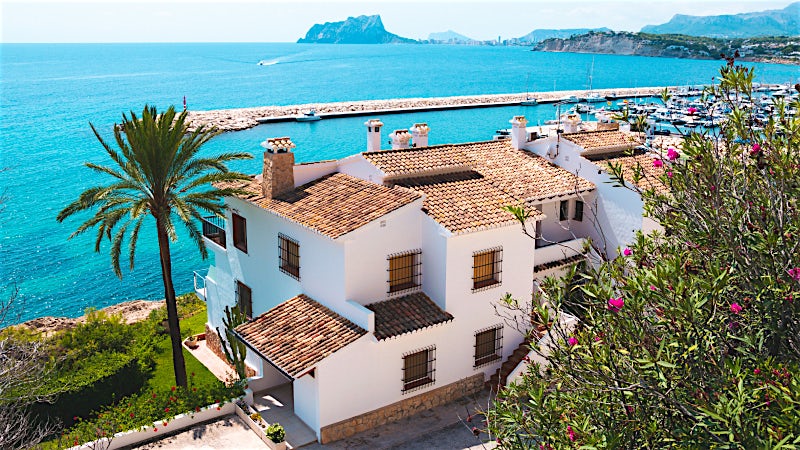 Costa Blanca seafront villa overlooking turquoise Mediterranean waters, marina, palm trees and scenic Spanish coastline views.