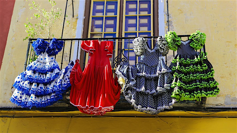 Traditional Spanish flamenco dresses hanging from a balcony, showcasing colorful ruffled costumes and Andalusian cultural heritage.